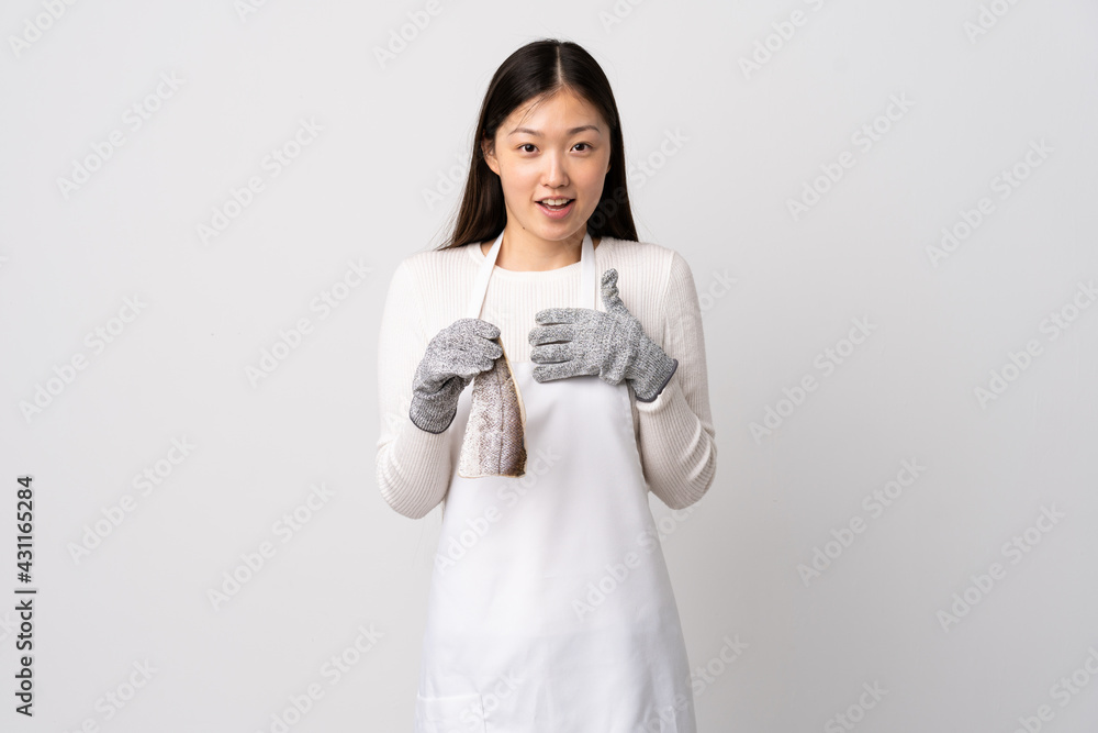 Chinese fishmonger wearing an apron and holding a raw fish over isolated white background pointing to oneself Chinese fishmonger wearing an apron and holding a raw fish over isolated white background pointing to oneself
