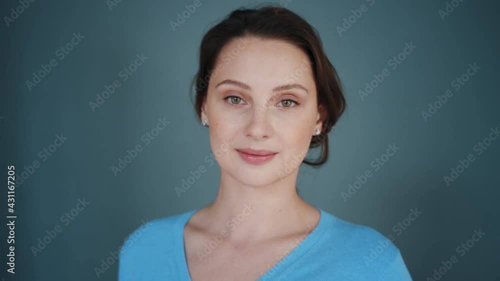 Beautiful smiling young caucasian woman with pretty face, gentle shy looking at camera and posing alone at home on blue background. Cute lovely portrait of happy young adult millenial girl Beautiful smiling young caucasian woman with pretty face, gentle shy looking at camera and posing alone at home on blue background. Cute lovely portrait of happy young adult millenial girl
