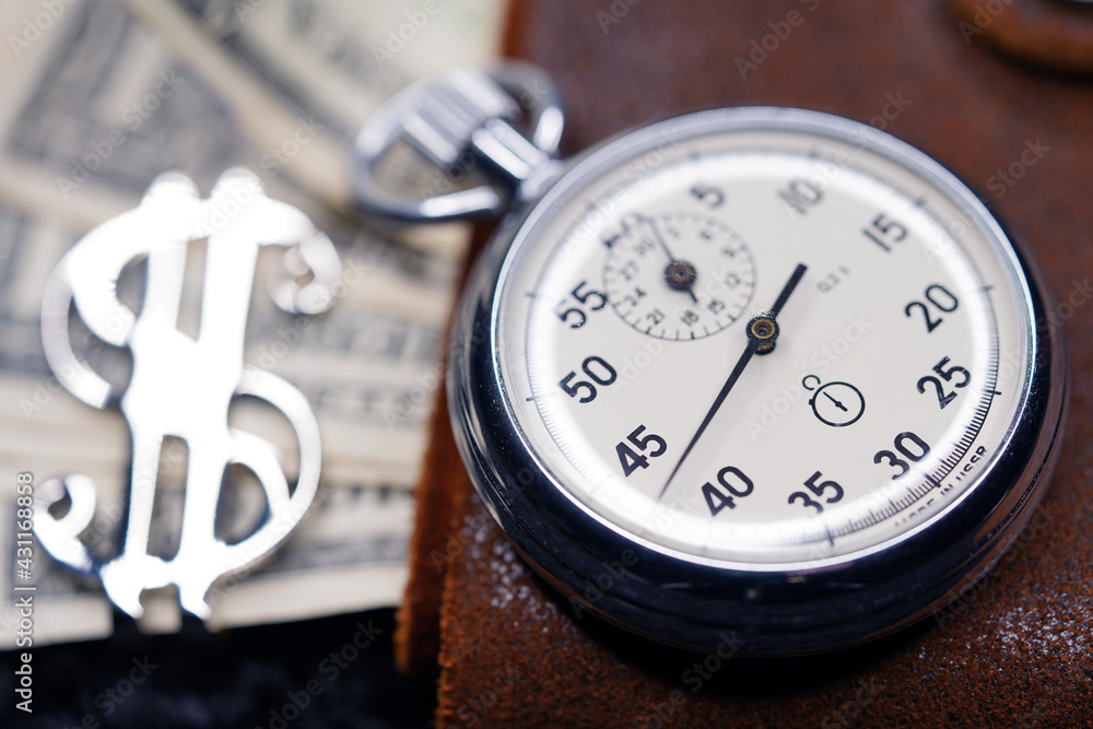 Dollar close-up. Money macro shot. The stopwatch lies on paper banknotes and a leather wallet. Clock, watch, timepiece, timer, clock face, mechanical device, speedometer Dollar close-up. Money macro shot. The stopwatch lies on paper banknotes and a leather wallet. Clock, watch, timepiece, timer, clock face, mechanical device, speedometer