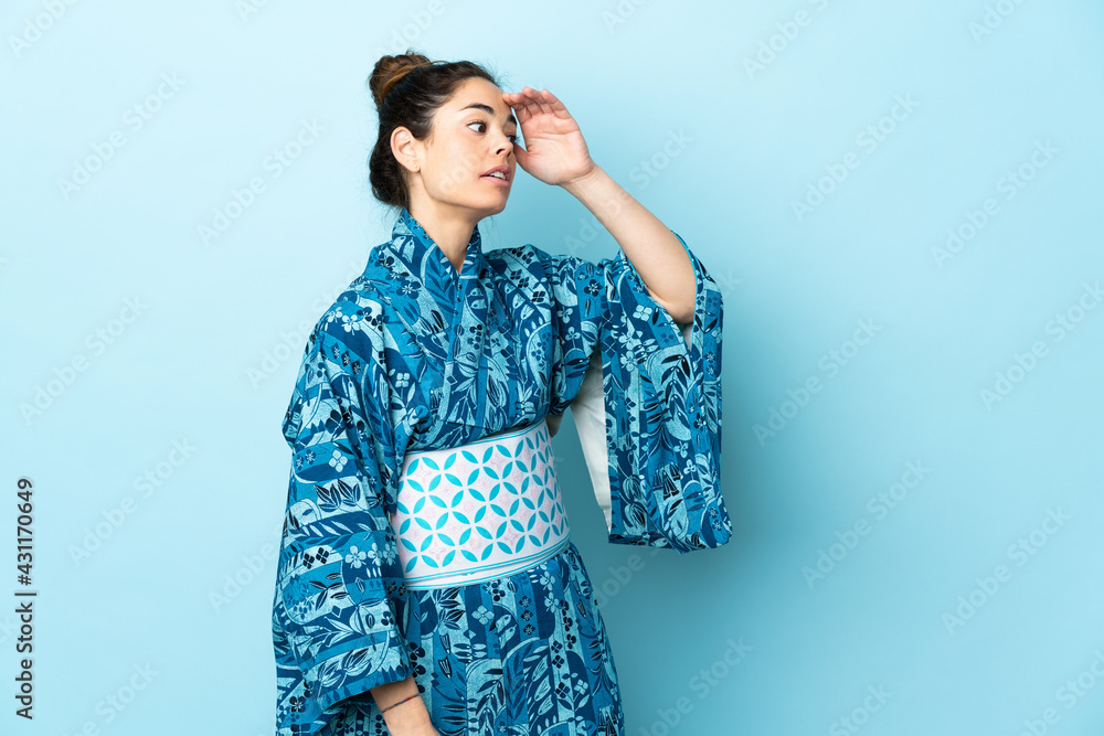 Woman wearing kimono over isolated background with surprise expression while looking side Woman wearing kimono over isolated background with surprise expression while looking side