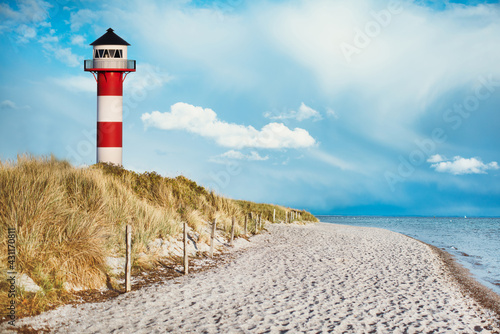 Leuchtturm am Strand einer Insel  Sylt  an der K  ste hinter und auf D  ne mit Strandsand und Wasser am Meer. blauer Himmel mit wei  en Wolken mit Platz f  r Text