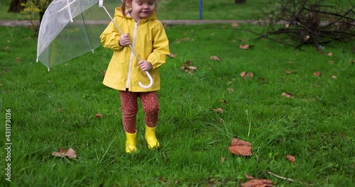 cute toddler girl in raincoat and boots walking on a fresh spring meadow at the city park photo