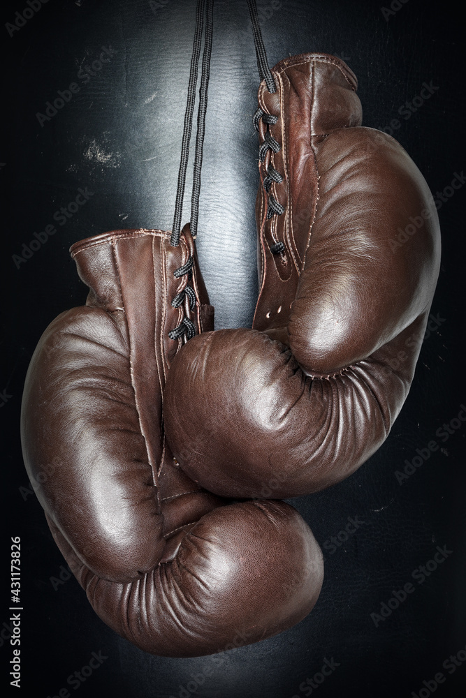 Brown leather boxing gloves lie on a black punching bag. Sport equipment. Training. The fight. Sparring                             