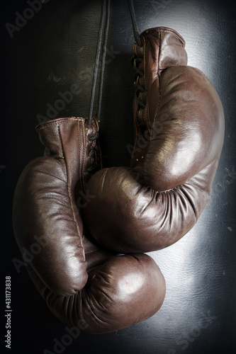 Brown leather boxing gloves lie on a black punching bag. Sport equipment. Training. The fight. Sparring                              © v75