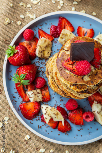 Healthy banana oatmeal pancakes stack with strawberries  bananas  raspberries and chocolate. Easy making gluten free morning breakfast or brunch. Delicious heap of pancakes with vibrant  fun  colors.