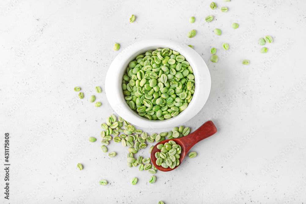 Bowl and spoon with green coffee beans on light background Bowl and spoon with green coffee beans on light background