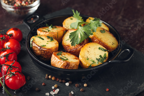 Frying pan of tasty fried potatoes with parsley and tomatoes on dark background