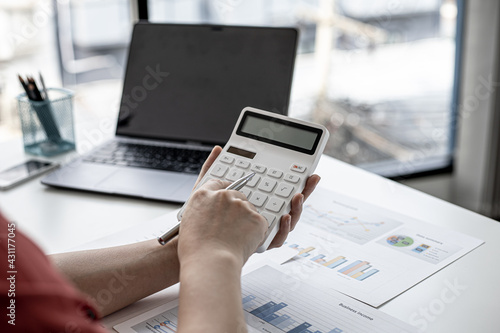 A close-up of a business finance woman's hand pressing a white calculator to calculate numbers from company financial documents. Concept of validating the accuracy of financial numbers.