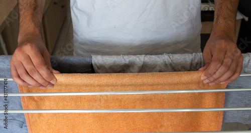 Fotografie Closeup shot of a man's hands hanging wet clothes on the indoor metal drying rac
