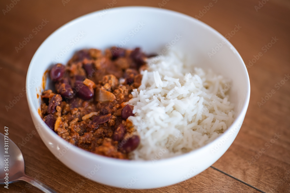 Close up and selective focus of meat chilli concarne and white rice in a white bowl on a wooden surface with intentional shallow depth of field and bokeh Close up and selective focus of meat chilli concarne and white rice in a white bowl on a wooden surface with intentional shallow depth of field and bokeh