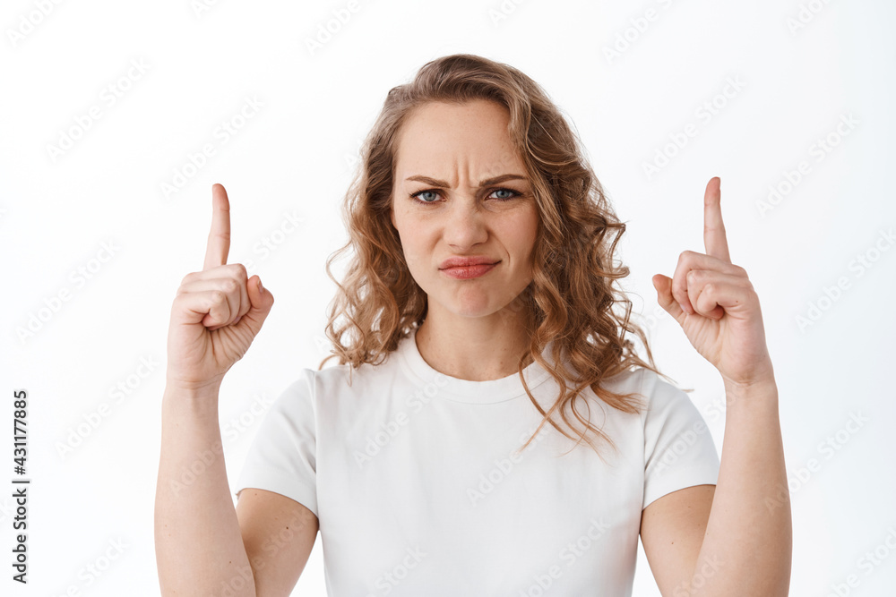 Displeased moody girl grimacing, look with dislike and aversion, pointing fingers up at cringe content, showing bad copyspace, white background Displeased moody girl grimacing, look with dislike and aversion, pointing fingers up at cringe content, showing bad copyspace, white background