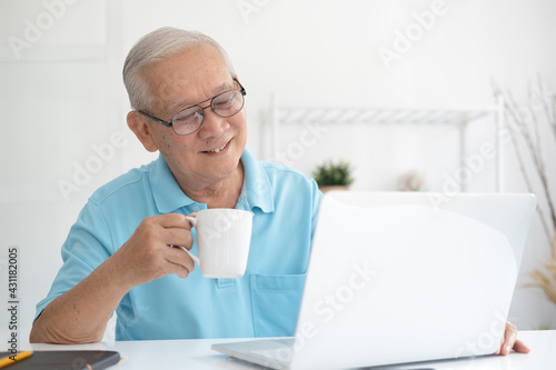 Happy senior man working on laptop and holding coffee cup