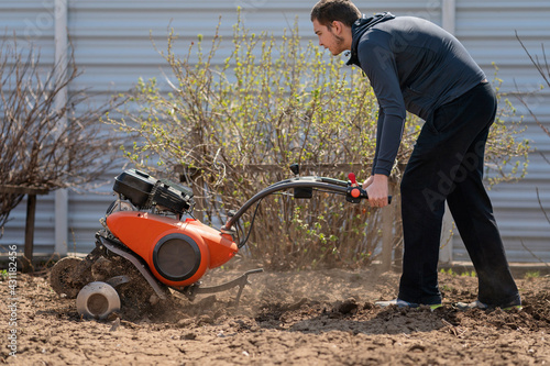 A young man digs the ground in the garden with a motorcultivator photo