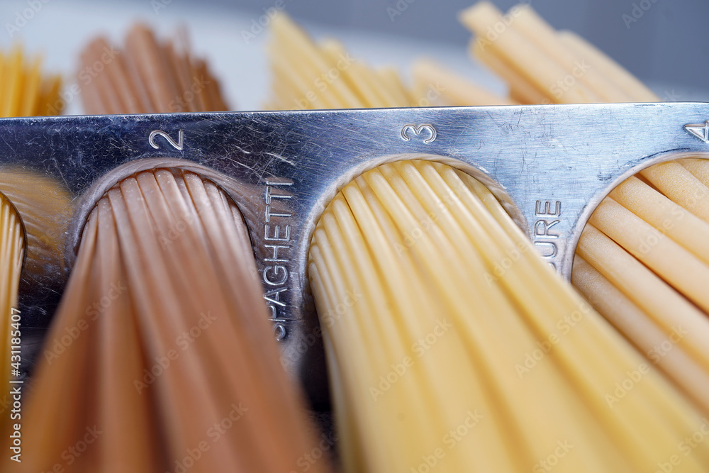 A measure of spaghetti with pasta in it lying on a black background. Close up.  Cooking. Metal kitchen tools. Batch measurement. Kitchenware. Pasta. Italian Cuisine                                    