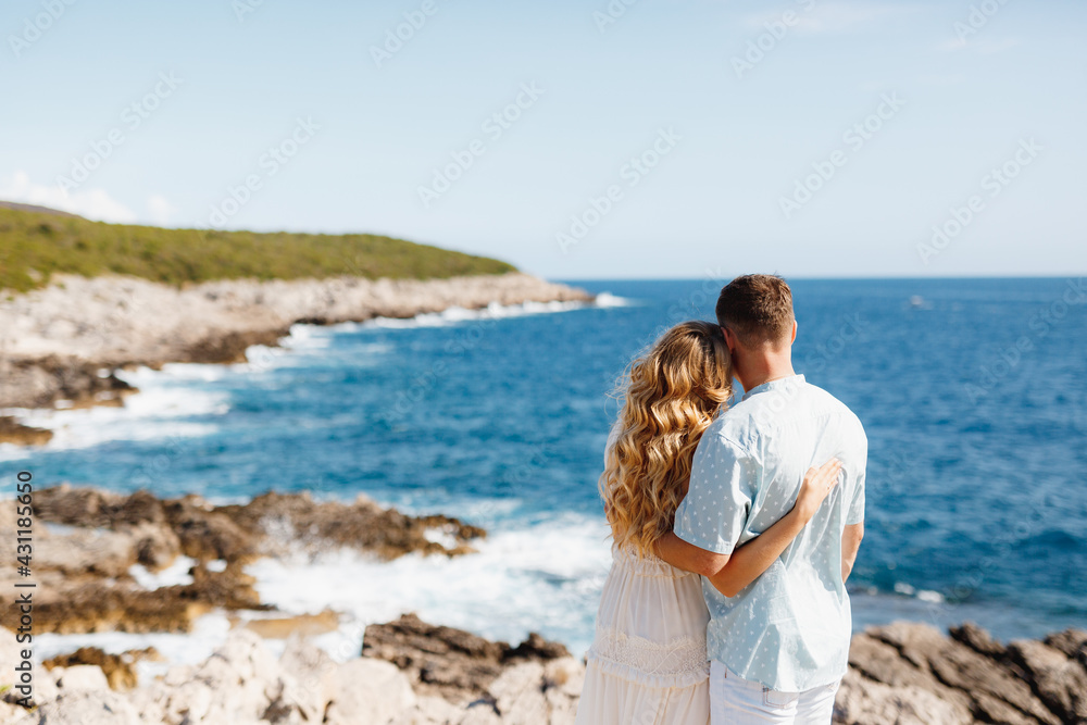Man and woman in love stand embracing on the rocky seashore, back view 