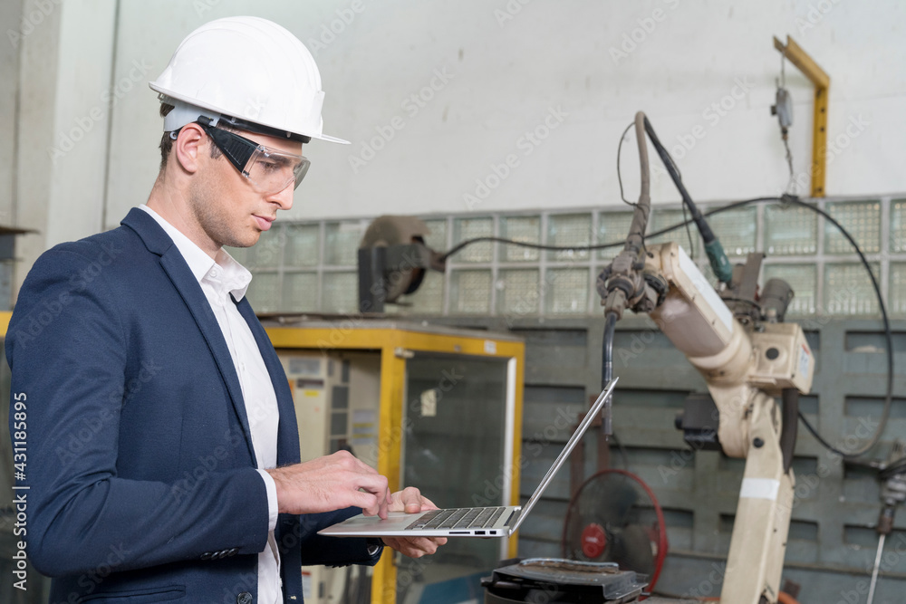 The engineer is explaining the operation of the machine. Man using laptop computer with robot arm production line. The engineer is explaining the operation of the machine. Man using laptop computer with robot arm production line.