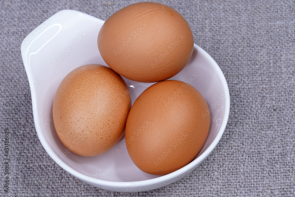 Three brown chicken eggs in a white round bowl top view. Eating raw foods. Proteins. Three brown chicken eggs in a white round bowl top view. Eating raw foods. Proteins.