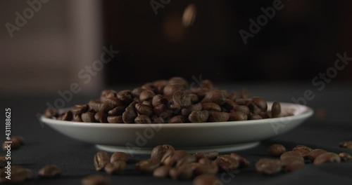 Close up of organic roasted coffee beans falling down in slow-motion shot at 120 fps on a white plate