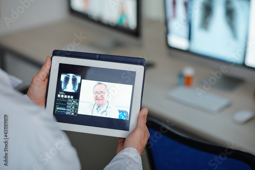 Doctor with tablet computer making videocall to experienced senior general practitioner from another clinic to get advice on difficult case