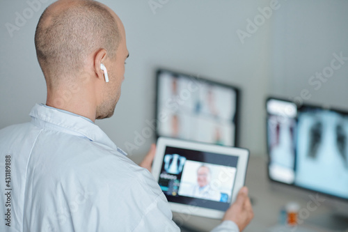 Physician wearing earbuds when making video call to his colleague from another clinic