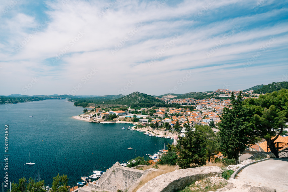 View of the sea and the pier with white yachts from behind the roofs of old houses in Sibenik. Side view