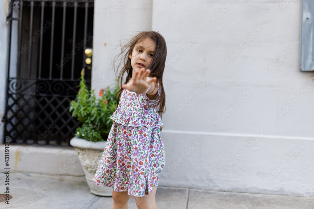 Beautiful little girl in flowered dress posing in front of a gray wall