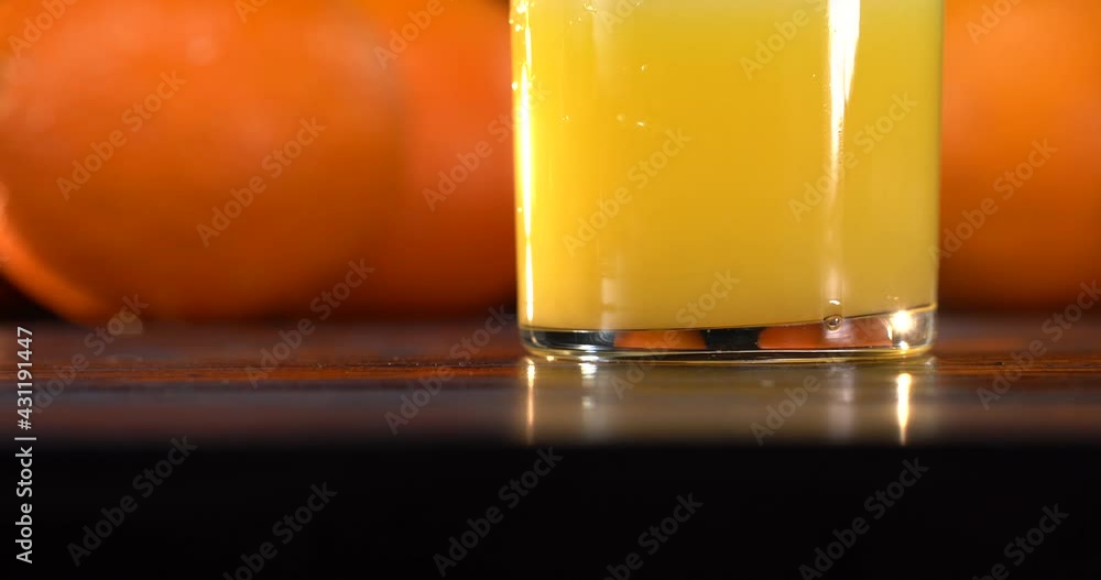 Orange juice is poured into a glass. there are fresh oranges on the table nearby. Dark table Orange juice is poured into a glass. there are fresh oranges on the table nearby. Dark table