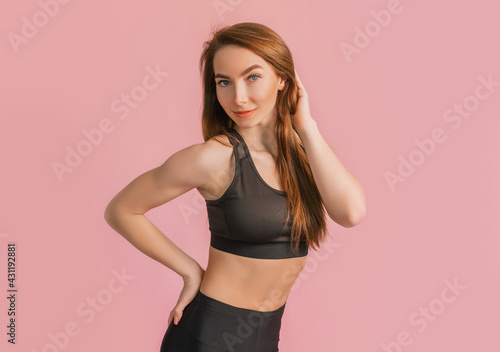 Fitness girl smiling in black sportswear on a pink background. Slim woman with a beautiful athletic body and tanned skin © Daria Lukoiko