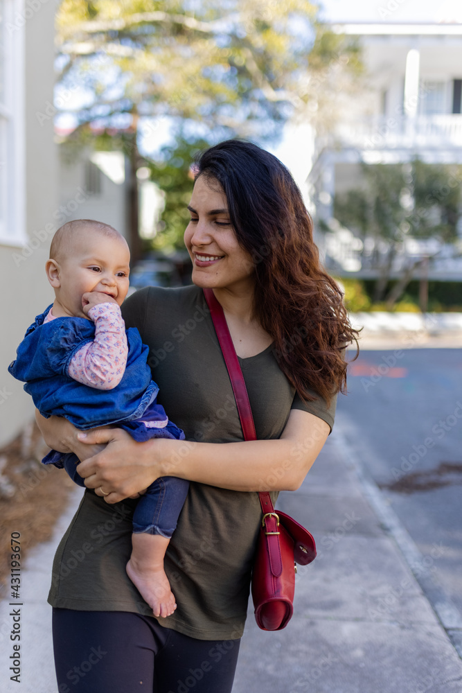 Fototapeta premium Happy mother holding her cute baby with blurry trees and houses as background