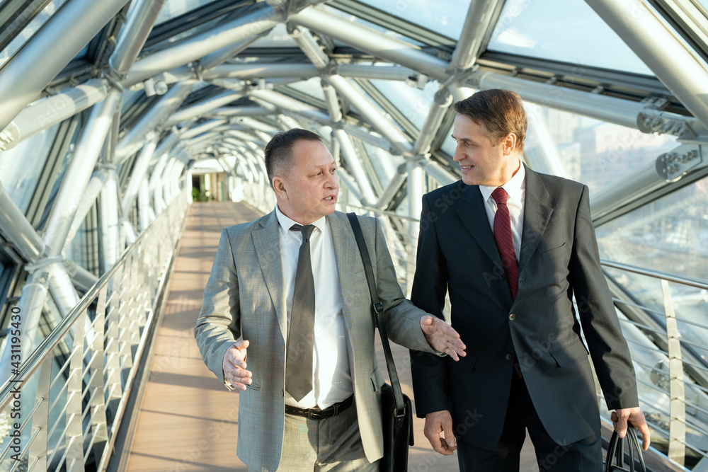 Two confident businessmen in suits walking along modern building Two confident businessmen in suits walking along modern building
