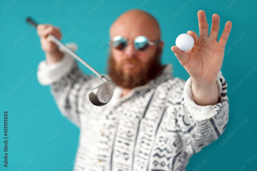 Naklejka premium A guy with a bald head and a lush beard holds in his hands a golf club and a ball. A man with glasses and a shirt. Golf player. Sports and Entertainment