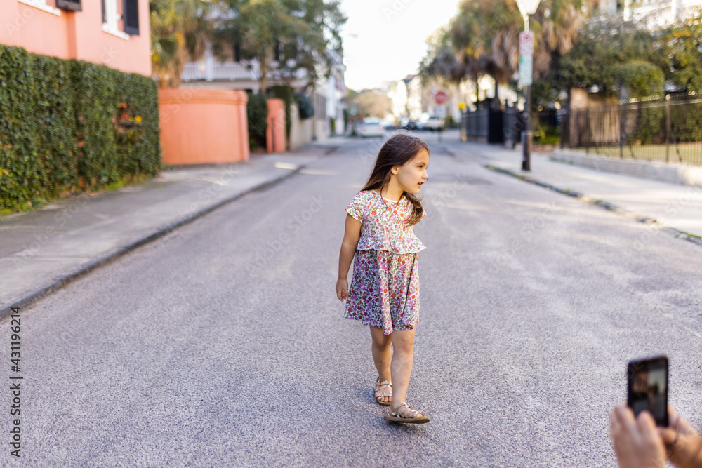 Naklejka premium Happy little girl in flowered dress slowly walking in empty street