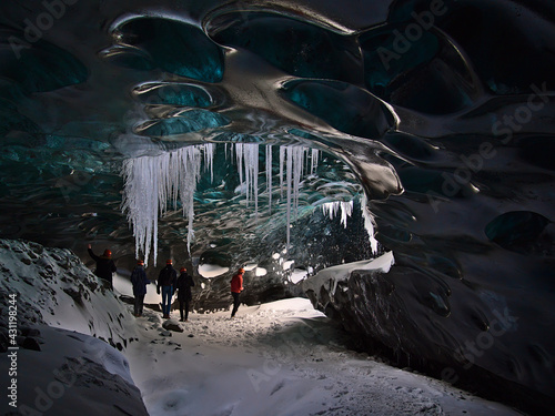 Group of tourists exploring the Sapphire Ice Cave, located in Breiðamerkurjökull glacier, Vatnajökull, Iceland, on a tour with a moulin hole in the blue shimmering ceiling and icicles hanging down.