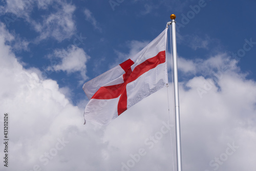 Red and white flag of St George England against blue cloudy sky