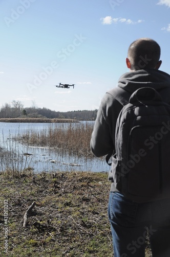 A man launches a drone. A man in a gray jacket and a gray backpack on the shore of a forest lake. Spring in nature. 