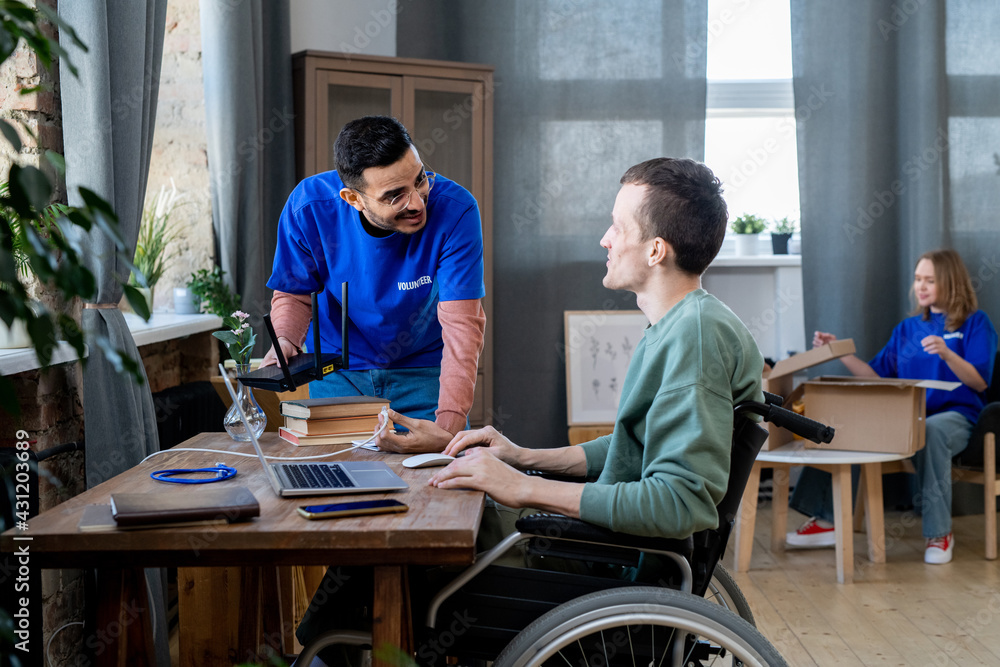 Young man in a wheelchair looking at volunteer with a woman in the background Young man in a wheelchair looking at volunteer with a woman in the background