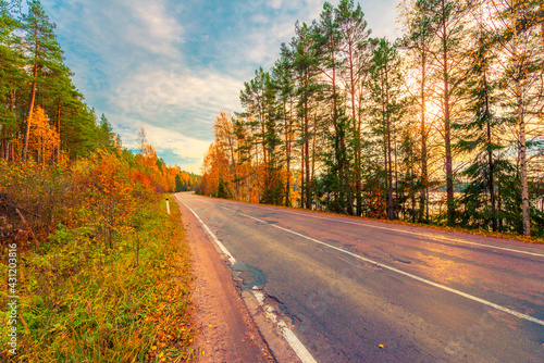 Turn the country broken road. Mixed forest. Sunset over the forest lake. Autumn weather. Beautiful nature. Russia, Europe. View from the side of the road.