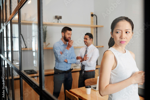 Serious young businesswoman eavesdropping on conversation of her male colleagues in meeting room photo