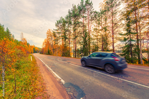 Turn the country broken road. The car goes on the road. Mixed forest. Sunset over the forest lake. Autumn weather. Beautiful nature. Russia, Europe. View from the side of the road.
