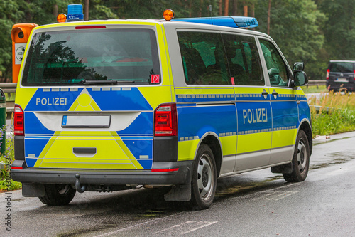German police car in an emergency stop on the highway next to an emergency telephone. Rainy weather and wet road surface. View of the vehicle body on the passenger side and the police lettering