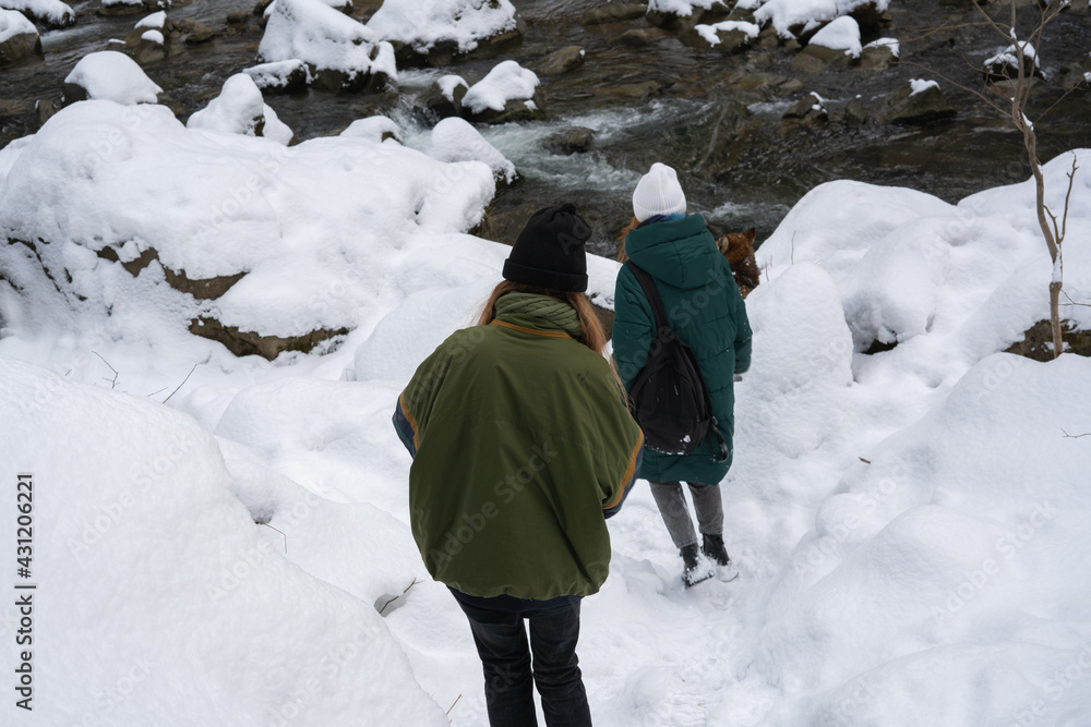A family of tourists on a hiking trail in the mountains covered in snow on the mountainside. Selective focus. Kamyanka waterfall. Carpathians. Ukraine.