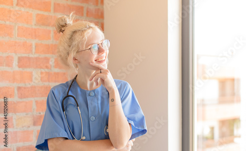 pretty nurse smiling with a happy, confident expression with hand on chin, wondering and looking to the side photo