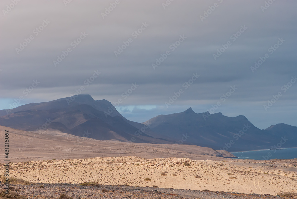 Picturesque mountain landscape with yellow send, colorful clouds and black peaks in nature park of Jandia Picturesque mountain landscape with yellow send, colorful clouds and black peaks in nature park of Jandia