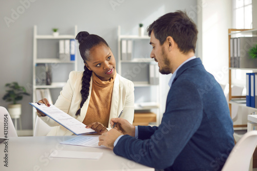 African american female solicitor pointing at insurance contract showing caucasian male client where to write signature. Sale purchase financial business deal, employment agreement, bank loan service