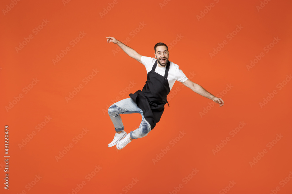 Full length young man barista bartender barman employee in black apron white tshirt work in coffee shop jump high outstretched hands legs isolated on orange background. Small business startup concept Full length young man barista bartender barman employee in black apron white tshirt work in coffee shop jump high outstretched hands legs isolated on orange background. Small business startup concept