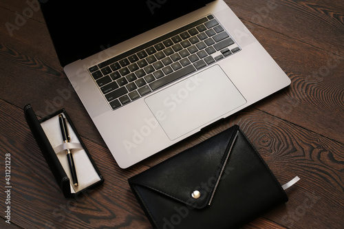 Closeup of laptop and black leather notebook with pen in case on wood background