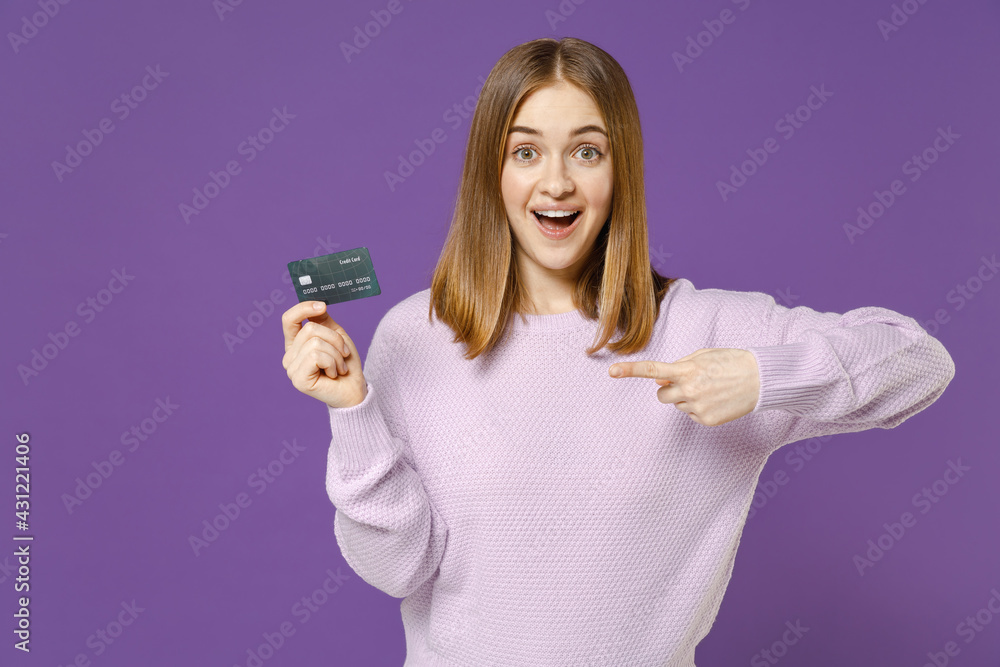 Young fun rich happy surprised student caucasian woman 20s wearing purple knitted sweater point index finger on credit bank card isolated on violet background studio portrait People lifestyle concept Young fun rich happy surprised student caucasian woman 20s wearing purple knitted sweater point index finger on credit bank card isolated on violet background studio portrait People lifestyle concept