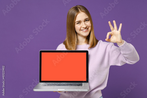 Young smiling positive happy freelancer student woman 20s in purple knitted sweater using laptop pc computer with blank screen workspace area show ok okay gesture isolated on violet background studio. © ViDi Studio