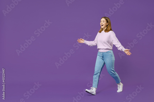 Full length young smiling fun surprised happy student caucasian woman 20s wear purple knitted sweater walk going spread hands isolated on violet background studio portrait People lifestyle concept.