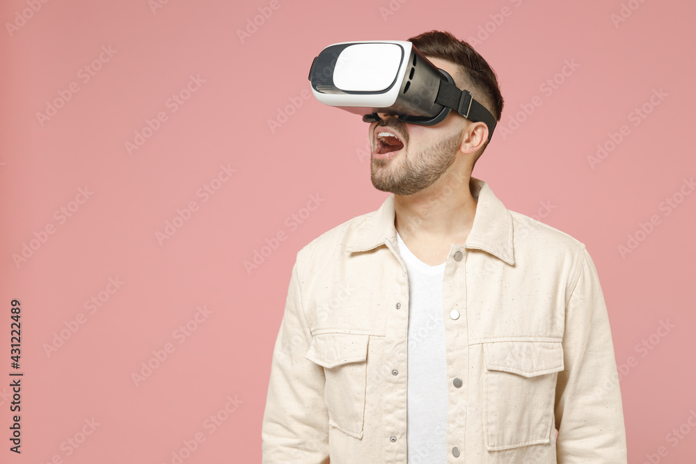Young happy fun amazed caucasian impressed man 20s wearing jacket white t-shirt watching in vr headset pc gadget isolated on pastel pink color background studio portrait. People lifestyle concept. Young happy fun amazed caucasian impressed man 20s wearing jacket white t-shirt watching in vr headset pc gadget isolated on pastel pink color background studio portrait. People lifestyle concept.